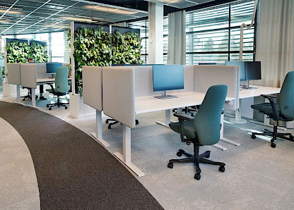 Trennwände aus Pflanzen sorgen im kreisförmigen Büro für Erfrischung. Die Arbeitsplätze sind mit ergonomischen Kinnarps Bürostühlen und Vibe Tischtrennwänden ausgestattet, um die Privatsphäre zu erhöhen und Umgebungsgeräusche zu dämpfen.